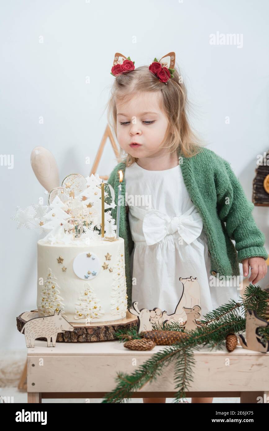 Décorations d'anniversaire d'hiver pour enfants. Jolie petite fille dans un  gilet vert près d'un gâteau d'anniversaire blanc Photo Stock - Alamy