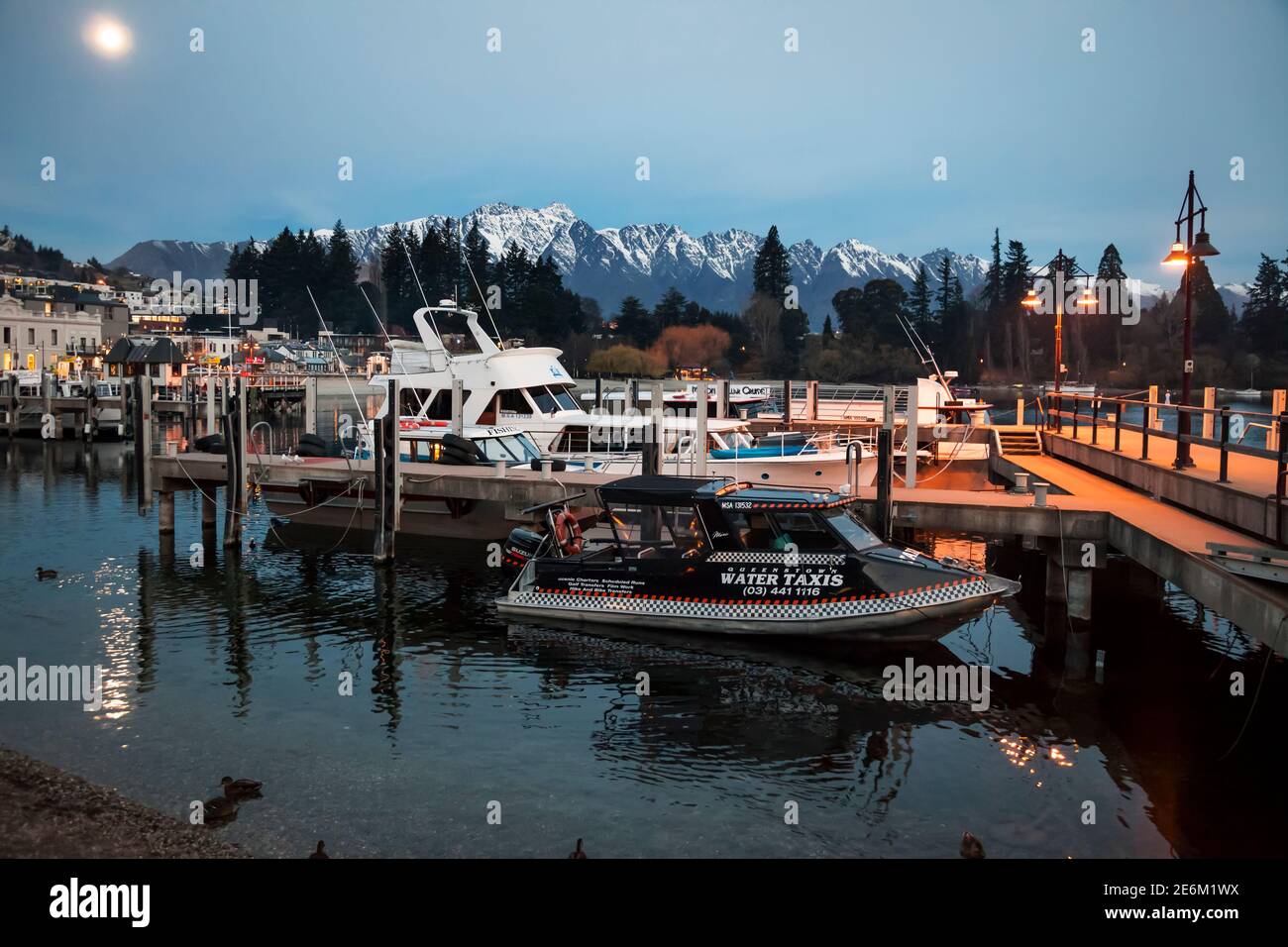 Quelques bateaux amarrés au bord de l'eau de la ville avec la chaîne de montagnes Remarkables en arrière-plan au coucher du soleil, Queenstown, South Island, Nouvelle-Zélande Banque D'Images