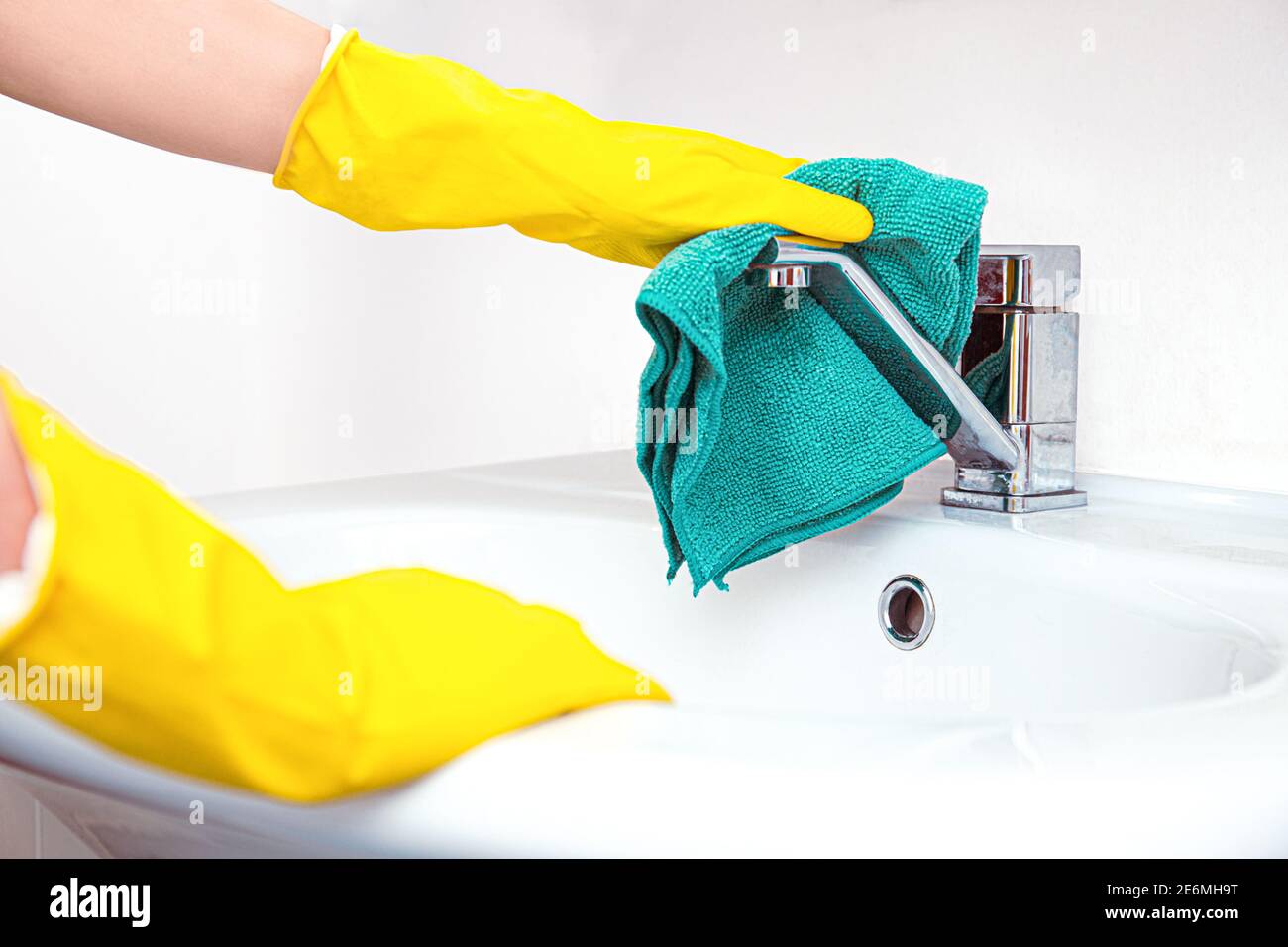 Nettoyez votre maison. Femme faisant des tâches dans la salle de bains, mains dans les gants jaunes nettoyage du robinet d'eau, évier en acier avec chiffon bleu et détergent spray Banque D'Images