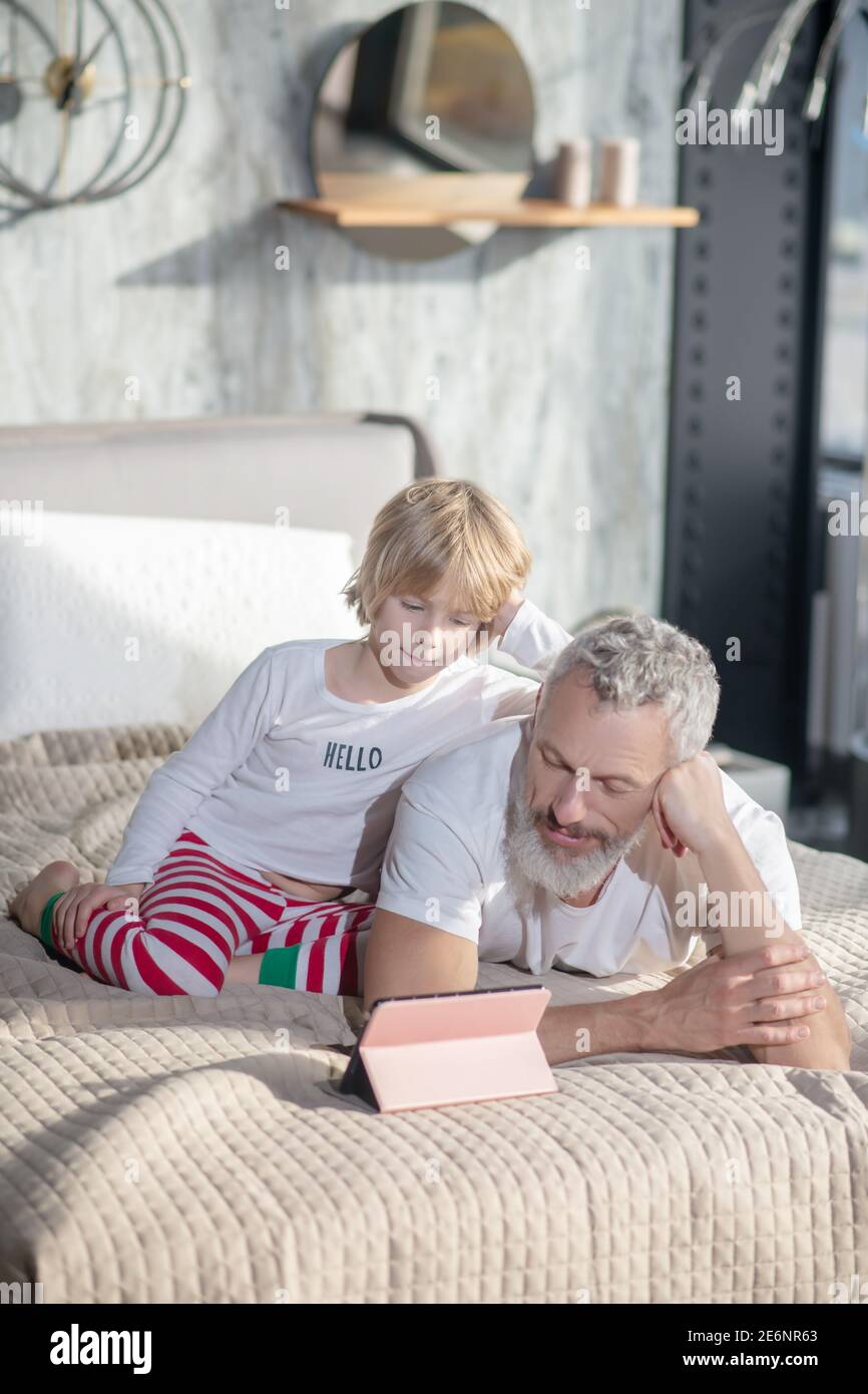 Bébé assis papa couché regardant la tablette Banque D'Images