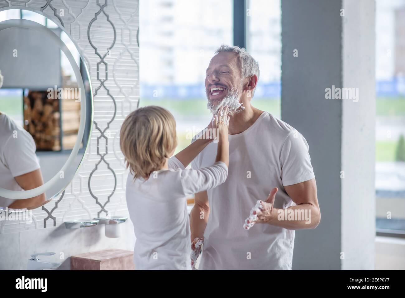 L'enfant se soulage de la barbe de ses pères avec des suds de savon Banque D'Images