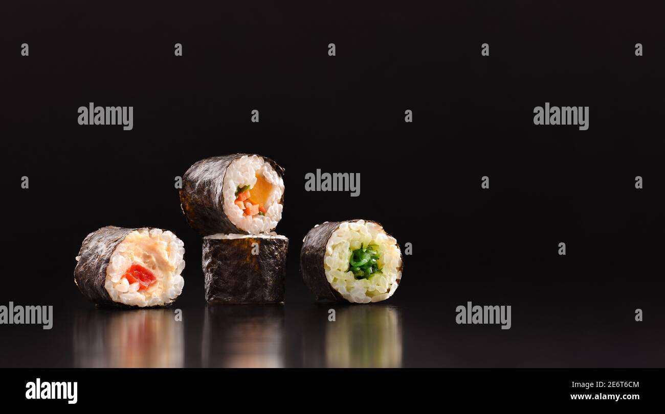 Arrière-plan avec quatre sushis maki aux légumes assortis sur une table en bois sombre avec fond noir. Vue avant. Composition horizontale. Banque D'Images