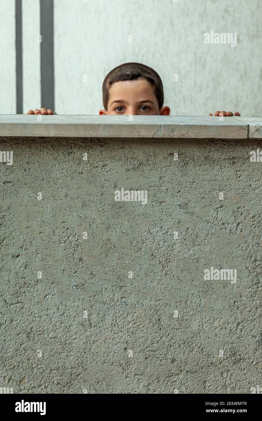Un garçon regarde derrière un mur bas Banque D'Images