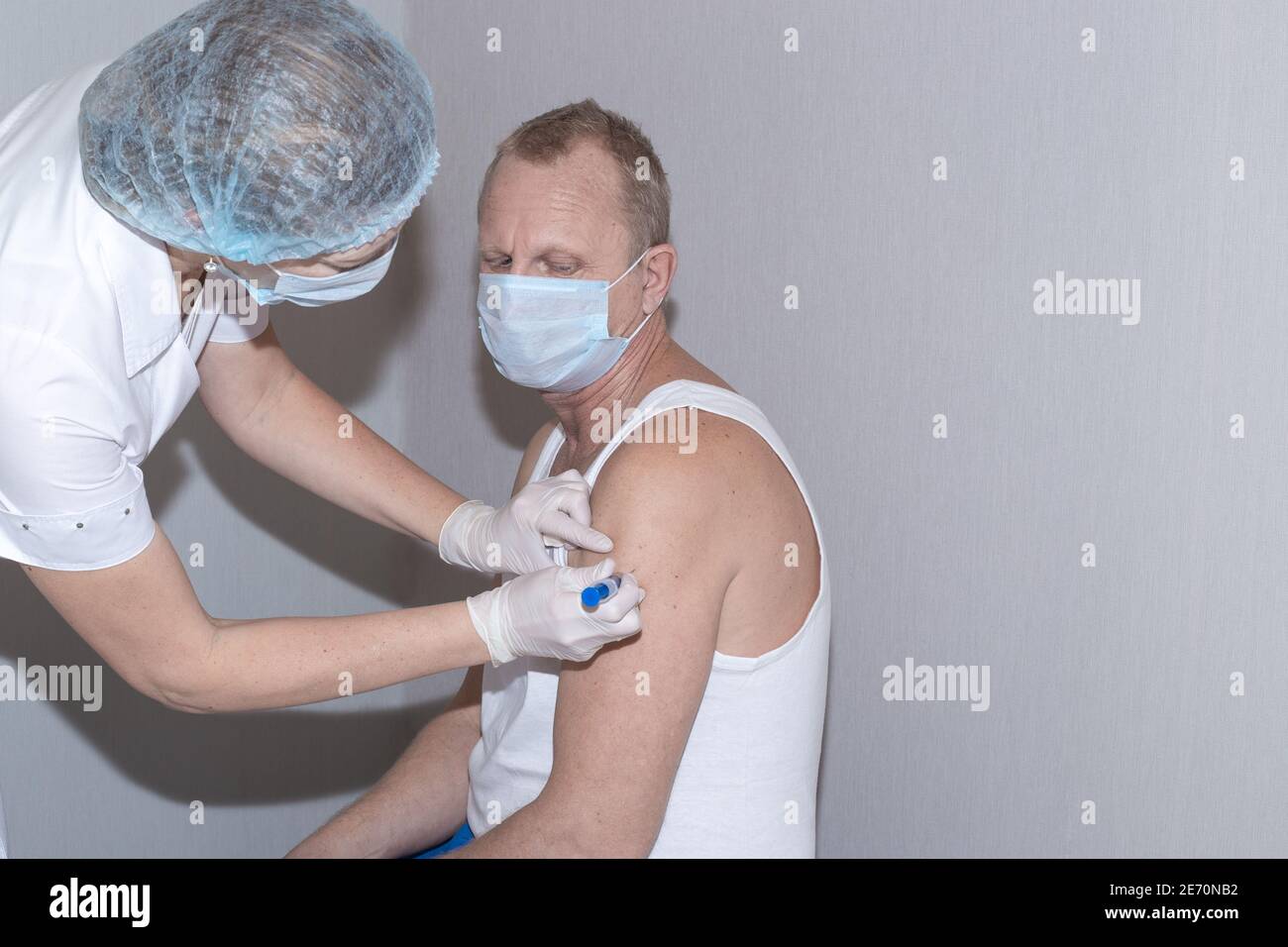 Vaccination contre le coronavirus. Une infirmière met le coup de feu dans l'épaule d'un homme mature portant un masque de protection. Immunisation de la population. Banque D'Images
