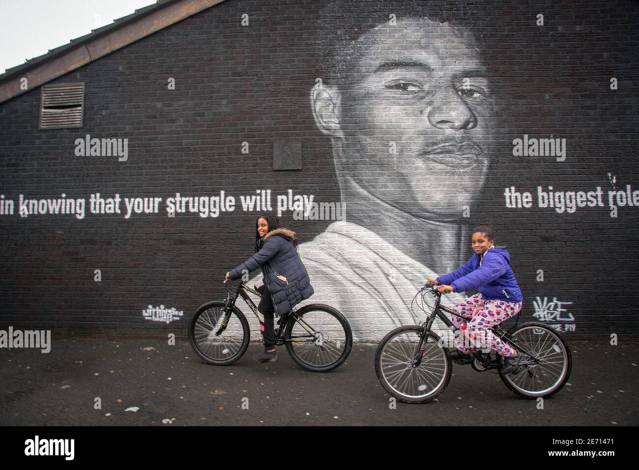 Deux enfants noirs sur des vélos passant devant la fresque du joueur de football de Manchester United Marcus Rashford sur le côté d'un bâtiment à Withington, Manches Banque D'Images