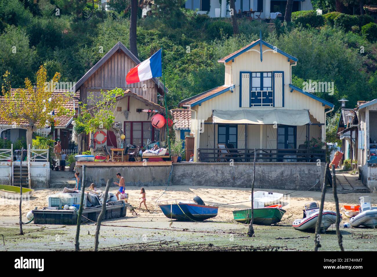Chalets typiques près du Cap Ferret dans le bassin d'Arcachon, France. En été, les bateaux ont été déferrés sur la côte en raison de la marée basse et d'un drapeau français Banque D'Images