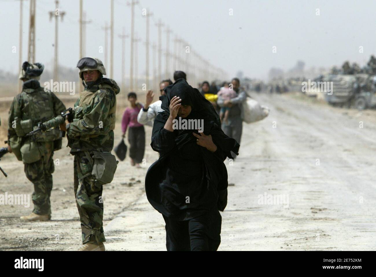 An Iraqi woman, a refugee from Baghdad, walks next to a U.S. Marine from Lima Company, a part of the 7th Marine Regiment, on the road south-east of the Iraqi capital April 5, 2003. U.S. Marine commander said on Saturday American troops would use overwhelming force to crush any resistance if ordered to storm Baghdad and that the battle would cost many civilian lives. REUTERS/Oleg Popov (IRAQ) Banque D'Images