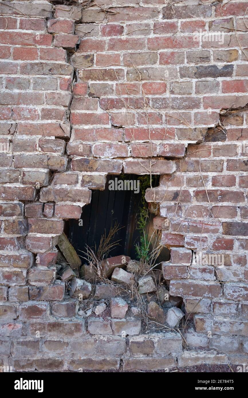 Photographie d'un vieux mur de briques en briques brisé poreux et ruiné mur de briques avec trou après accident, de nombreuses fissures, effondrement, arrière-plan sombre, vertical. Banque D'Images
