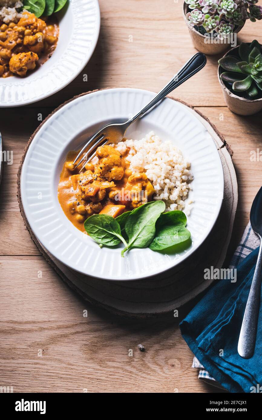 Curry de pois chiches et de chou-fleur avec riz brun et épinards sur fond de bois. Banque D'Images