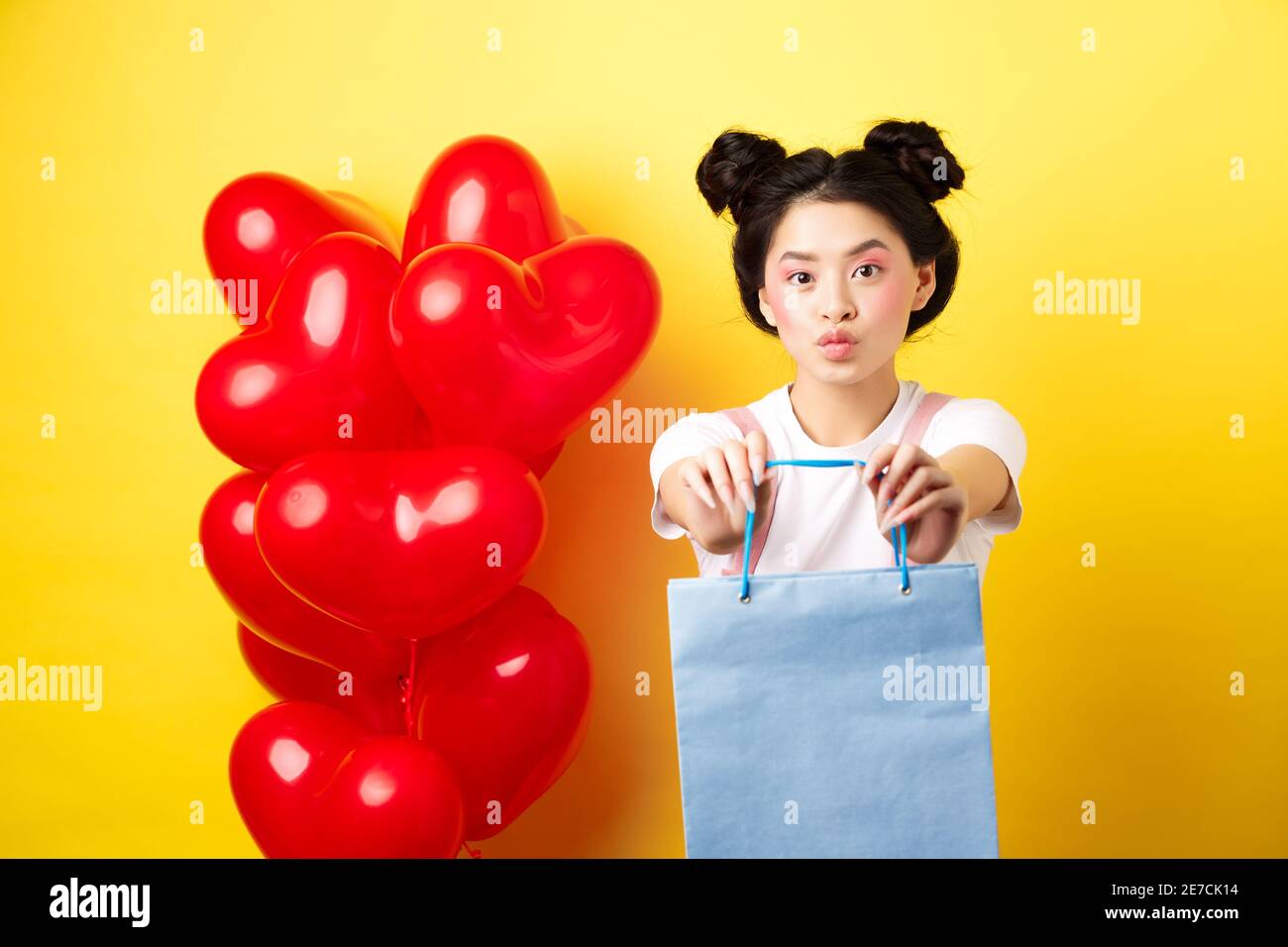 Bonne Saint Valentin. Adorable petite amie asiatique donnant à l'amant un  cadeau, étirez les mains avec un sac à provisions et l'air stupide, debout  sur jaune Photo Stock - Alamy