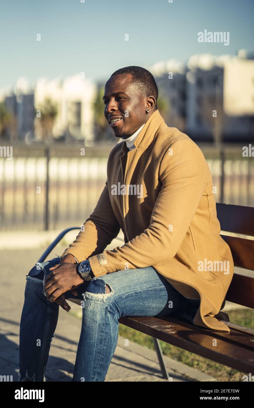 Plan vertical d'un styli beau sourire africain homme dedans un manteau  assis sur un banc Photo Stock - Alamy
