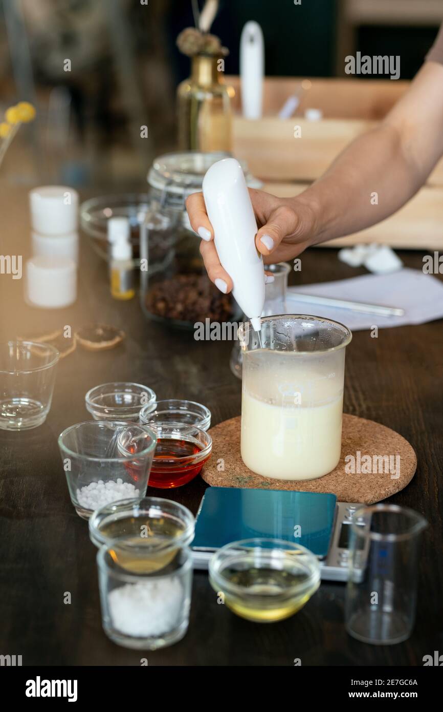 Main de la femme mettant la substance liquide transparente dans la verrerie avec masse de savon fondue tout en faisant le mélange pour les cosmétiques faits à la main Banque D'Images