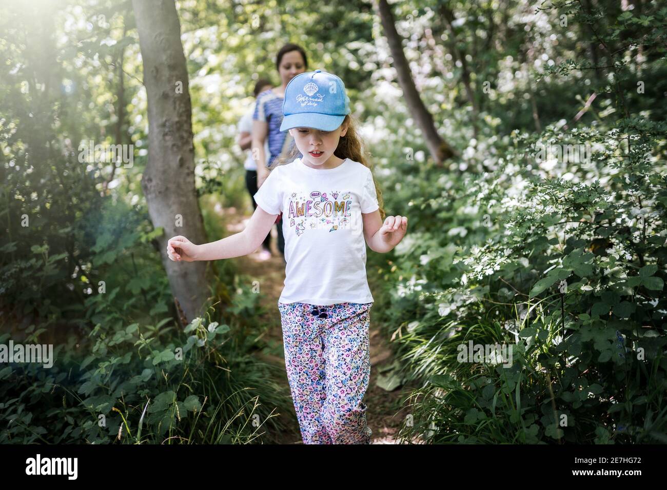 Jeune fille à cheveux longs en t-shirt et casquette de baseball marche à  travers la forêt boisée au soleil avec des rayons du soleil et maman en  arrière-plan Photo Stock - Alamy