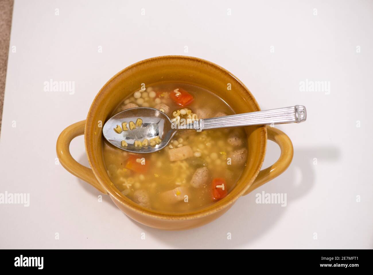 Une cuillerée de soupe à l'alphabet de nouilles de poulet indique « PORTER UN MASQUE ». Studio sur blanc. Banque D'Images