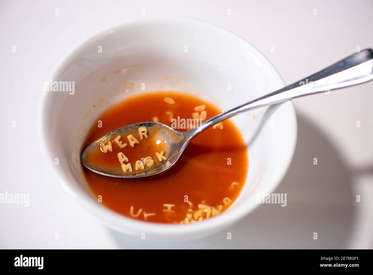 Une cuillerée de soupe à l'alphabet de tomate indique « PORTER UN MASQUE ». Studio sur blanc. Banque D'Images