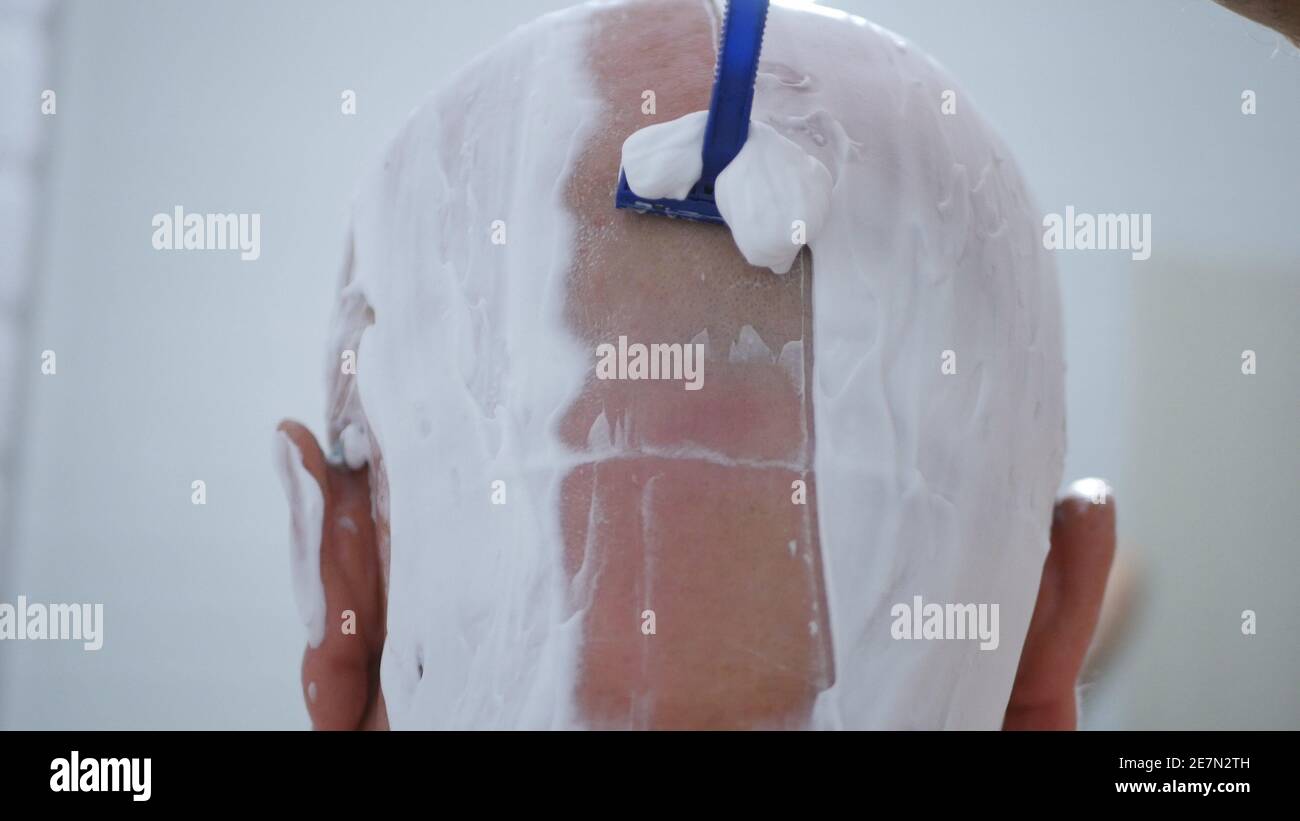 Homme dans la salle de bains se raser la tête avec un rasoir pointu Lame et mousse blanche Banque D'Images