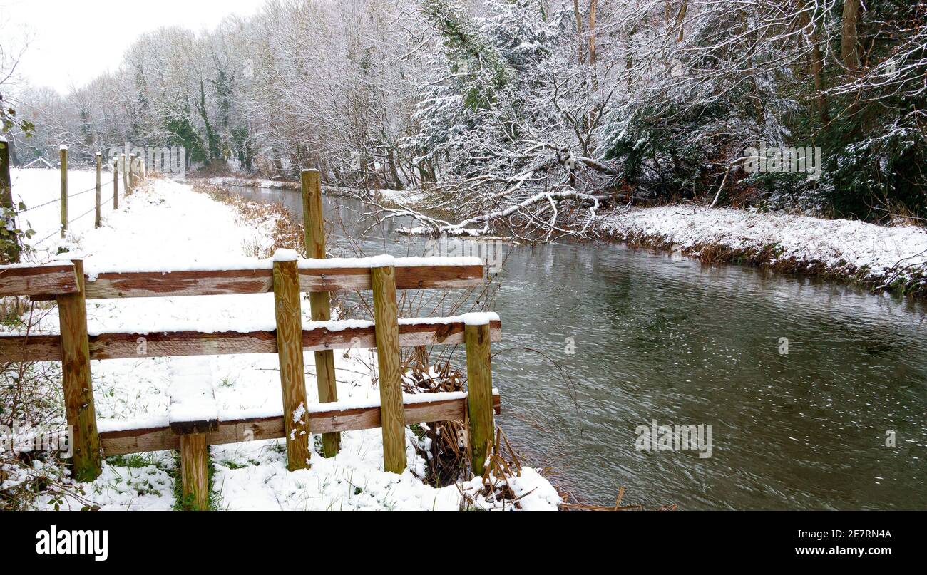 vue pittoresque en hiver le long d'une rivière avec des berges enneigées et une partie d'arbre tombée submergée dans le flux Banque D'Images