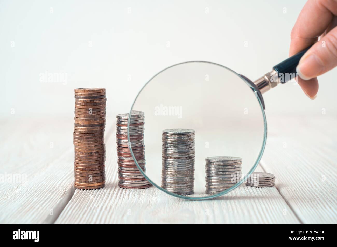 Une main avec une loupe examine les pièces en piles sur un fond clair. Banque D'Images