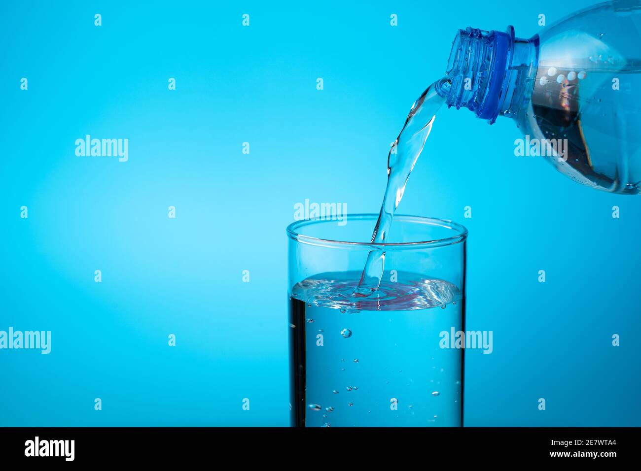 Un verre rempli d'eau d'une bouteille en plastique sur fond bleu. Banque D'Images