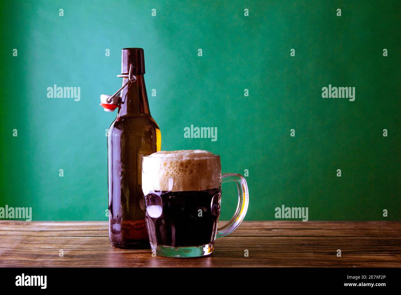 Une tasse de bière foncée avec sa bouteille ouverte sur fond vert et une table en bois. St. Patrick et Stout concept Banque D'Images