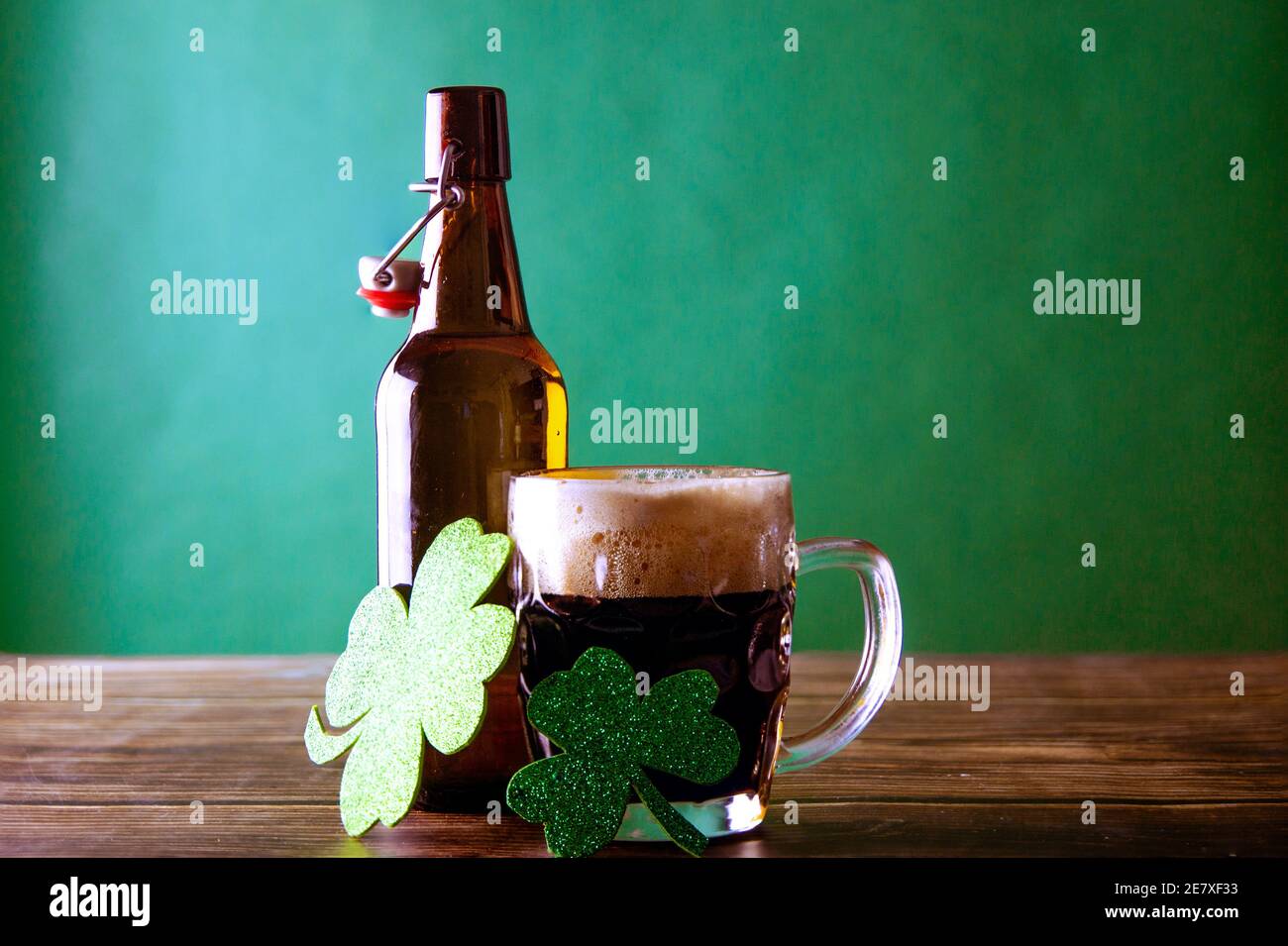 Une tasse de bière foncée avec sa bouteille ouverte sur un fond vert et une table en bois, à côté d'eux deux feuilles brillantes de trèfle vert symbole de Bonne chance. Banque D'Images