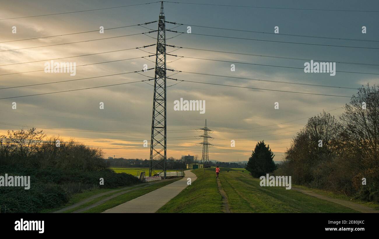 Les pylônes d'électricité sont répartis dans le champ pendant un jogger court le long d'une digue au coucher du soleil Banque D'Images