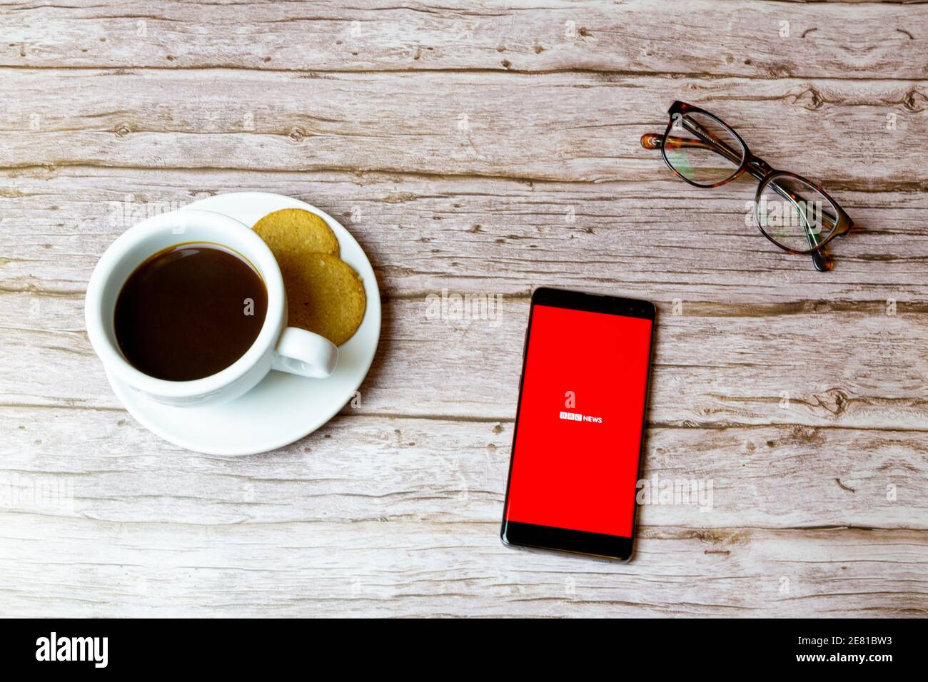 Un téléphone portable ou mobile posé sur un bois Table avec l'application BBC News qui ouvre également un café et lunettes Banque D'Images