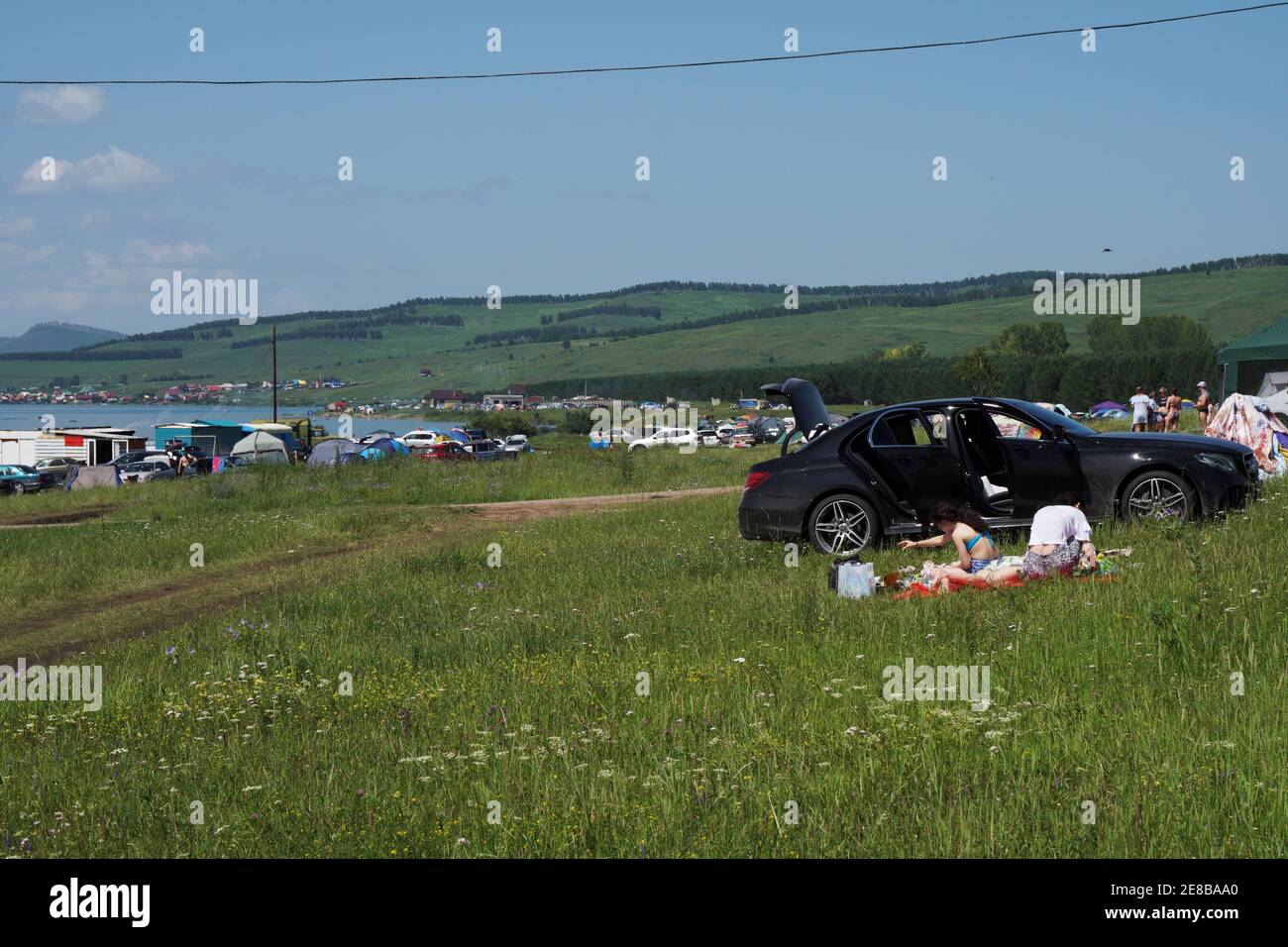 Les gens se reposent dans une aire de camping avec des tentes et des voitures sur une grande plage sur la rive du Grand lac. Banque D'Images