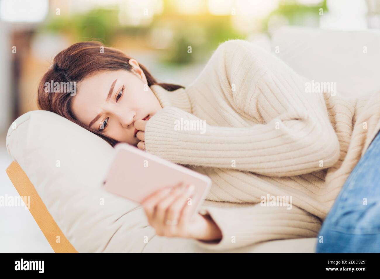 Une jeune femme stressée, couchée sur un canapé et regardant le téléphone portable Banque D'Images