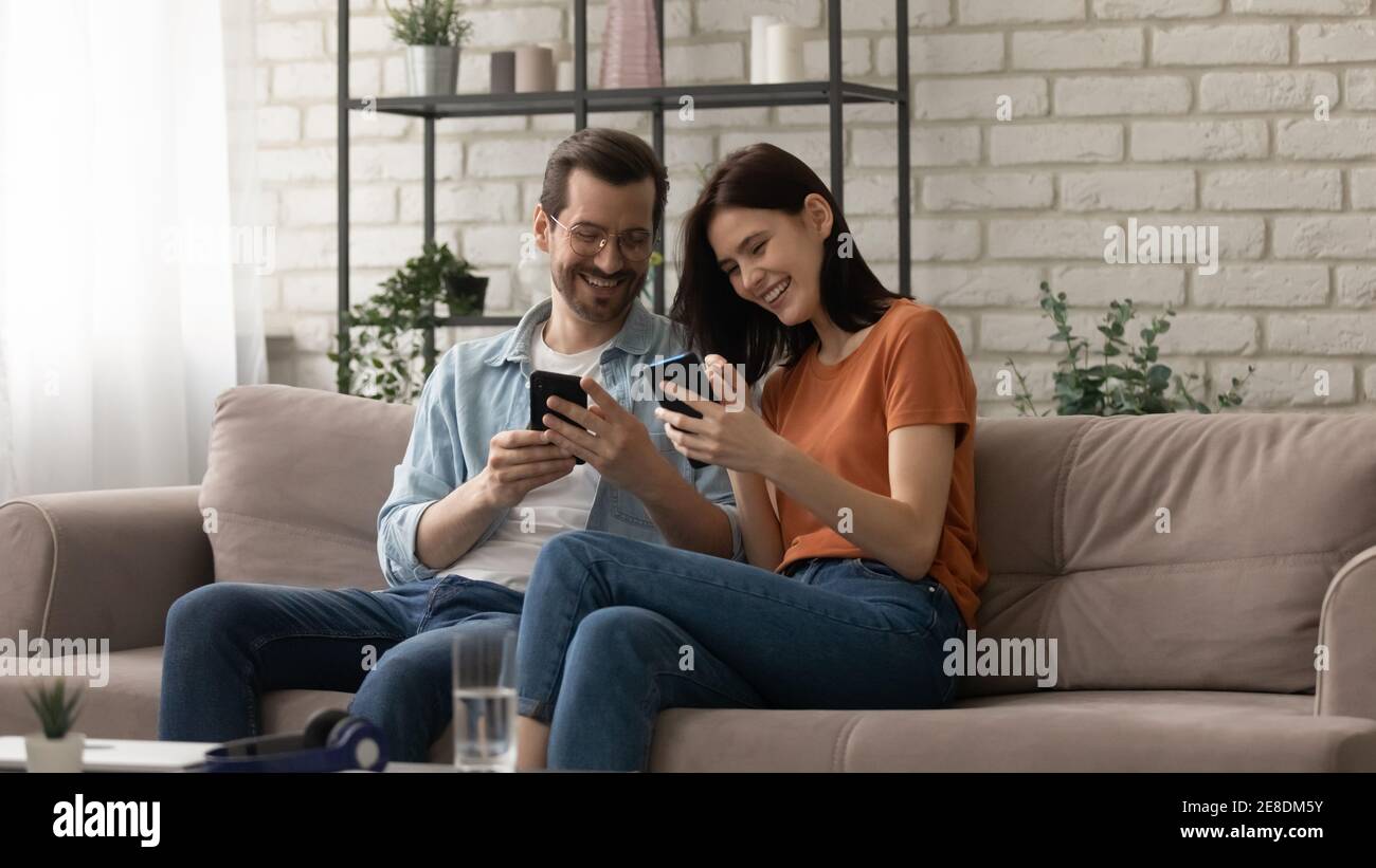 Couple surjoyeux utilisant des téléphones ensemble, assis sur un canapé confortable Banque D'Images