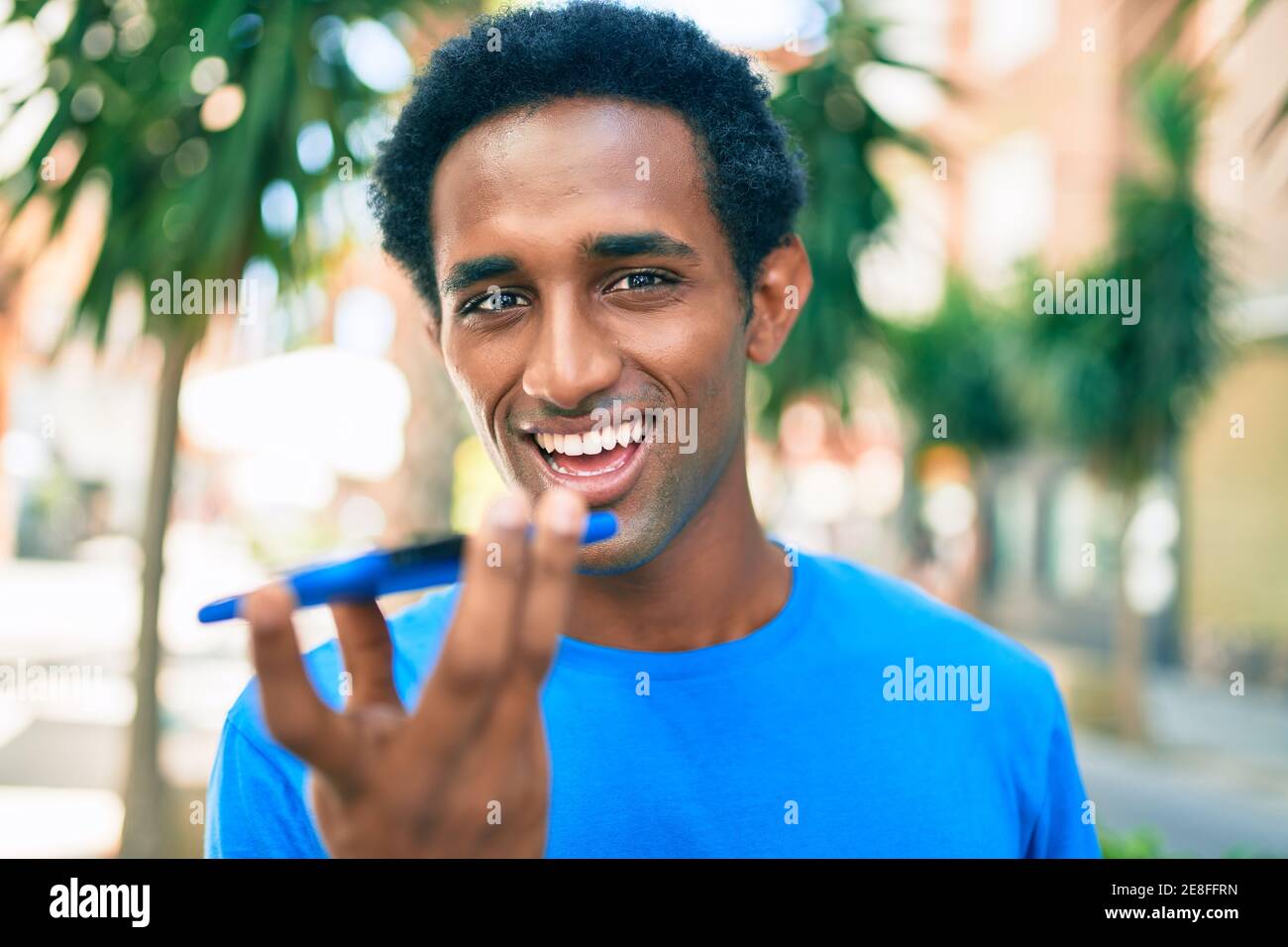 Beau noir africain homme souriant heureux plein air envoyer une voix message Banque D'Images