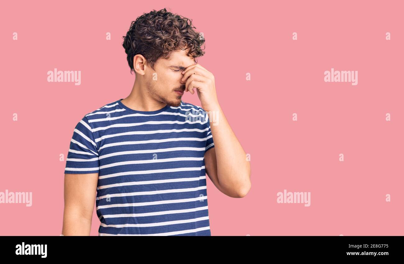 Jeune homme beau avec des cheveux bouclés portant des vêtements décontractés fatigués frottant le nez et les yeux sensation de fatigue et de maux de tête. Concept de stress et de frustration. Banque D'Images