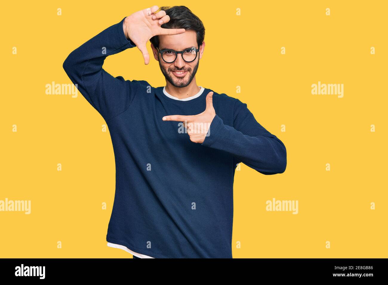 Jeune homme hispanique portant des vêtements et des lunettes décontractés souriant faisant cadre avec les mains et les doigts avec le visage heureux. Créativité et concept de photographie. Banque D'Images