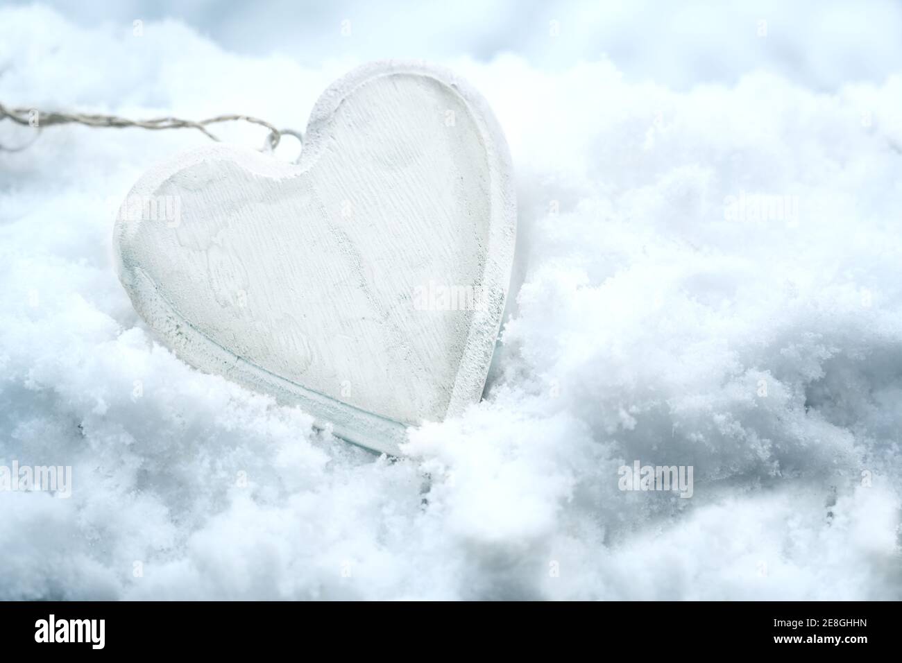 Coeur en bois peint en blanc couché dans la neige, symbole d'amour hivernal saisonnier pour le jour de la Saint-Valentin, le nouvel an ou les rismas, espace de copie, mise au point sélectionnée, Banque D'Images