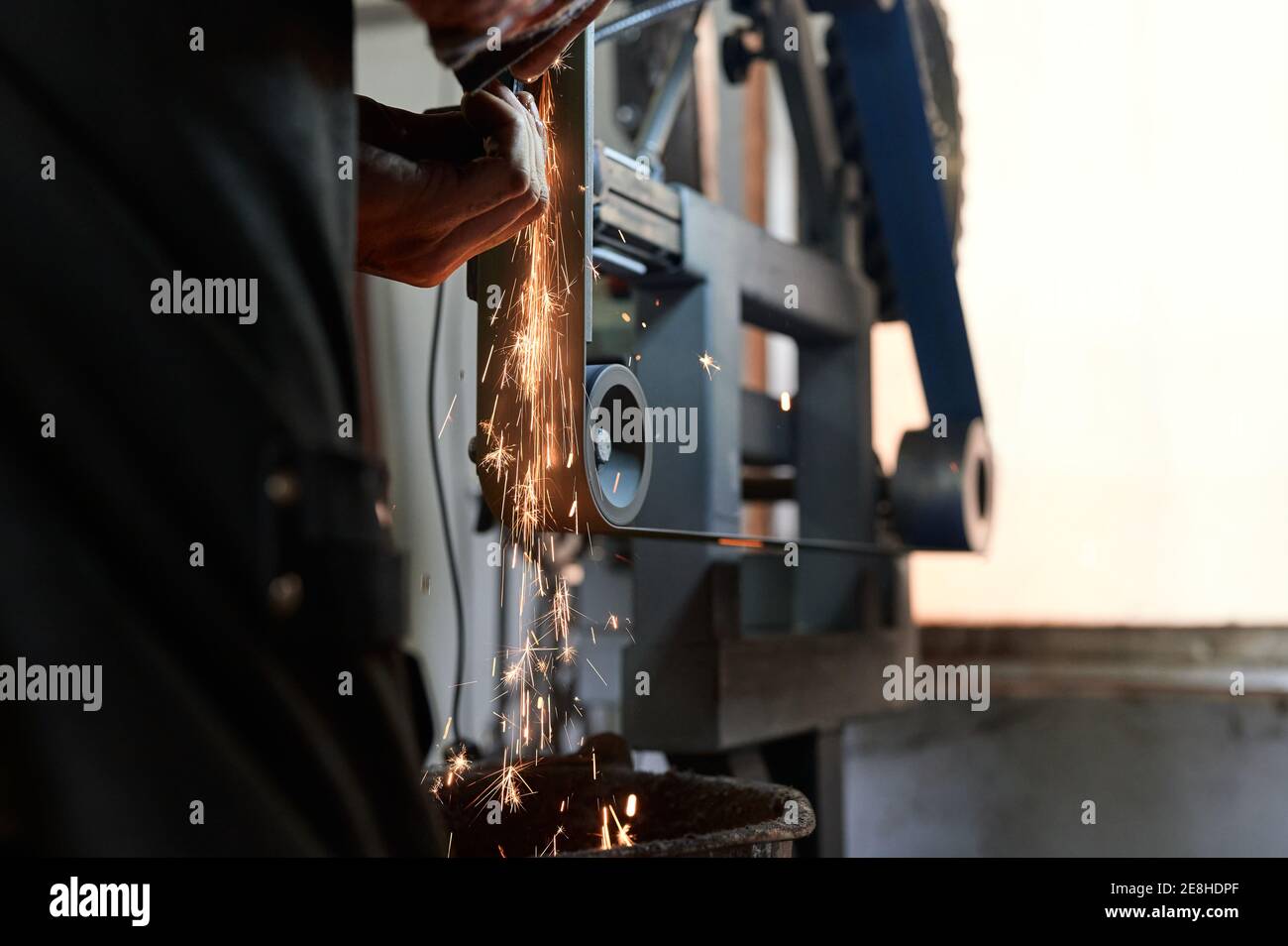 Vue arrière de jeune homme tatoué de forgeron en protection lunettes de protection et masque de polissage de petits détails métalliques sur la machine à meuler dans le bt Banque D'Images Vue arrière de jeune homme tatoué de forgeron en protection lunettes de protection et masque de polissage de petits détails métalliques sur la machine à meuler dans le bt Banque D'Images
