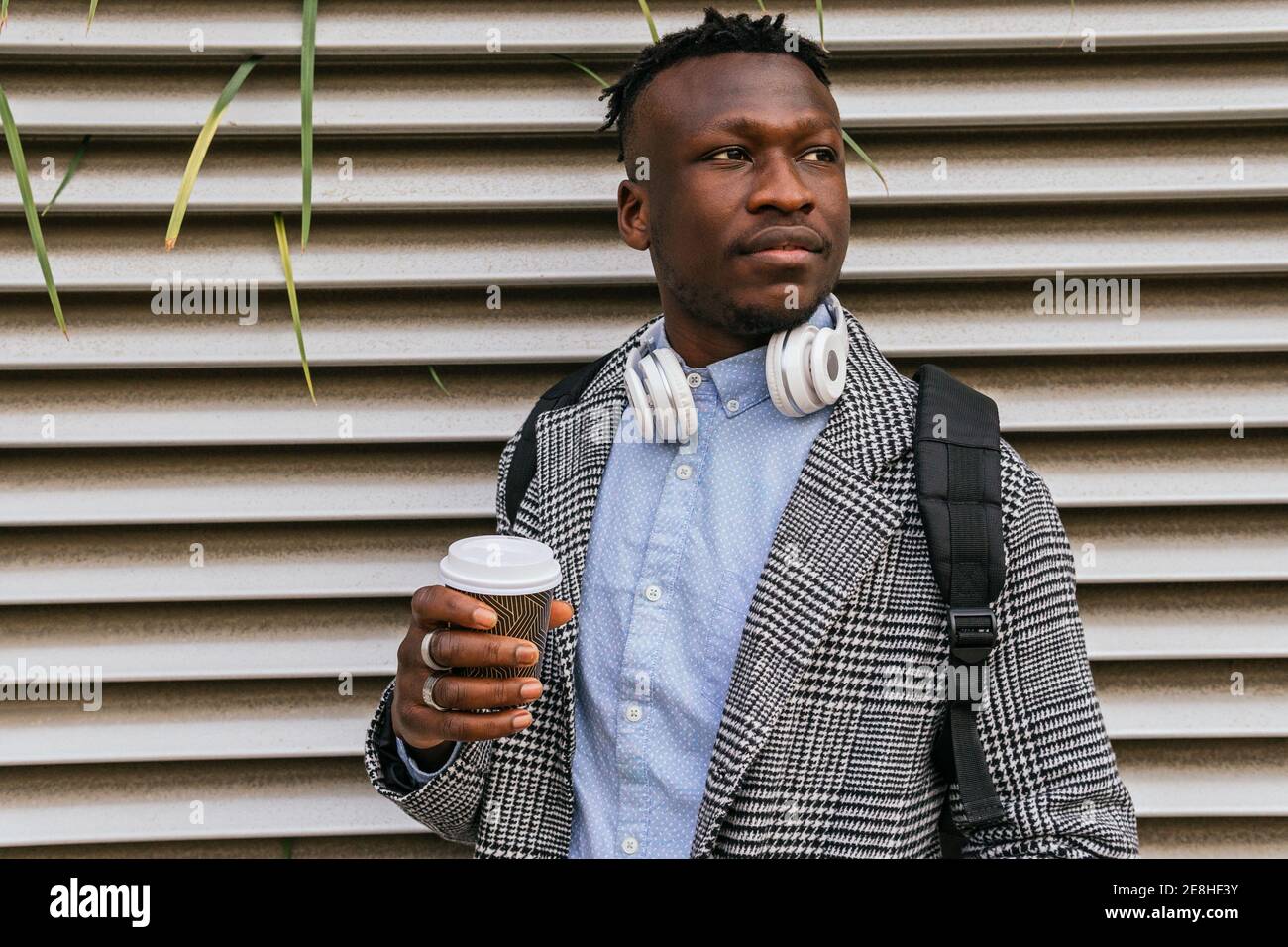 Jeune employé de bureau noir contemplatif avec micro-casque et à emporter café près du mur à côtes de la ville Banque D'Images