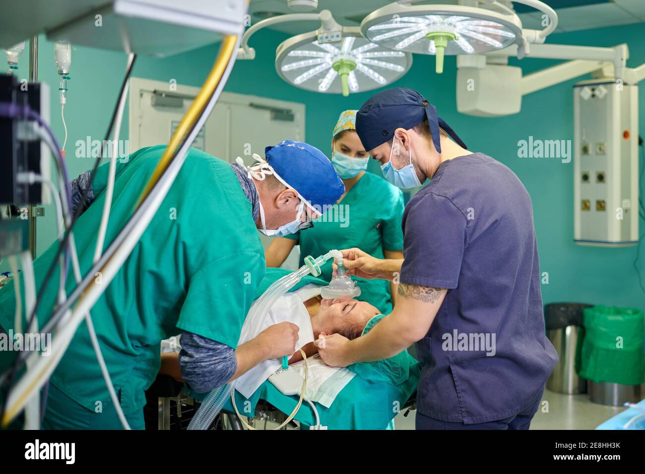 Vue latérale de l'anesthésiste mâle anonyme en uniforme médical et capuchon tenant le masque d'anesthésie sur le visage d'un patient allongé méconnaissable sur table en op Banque D'Images