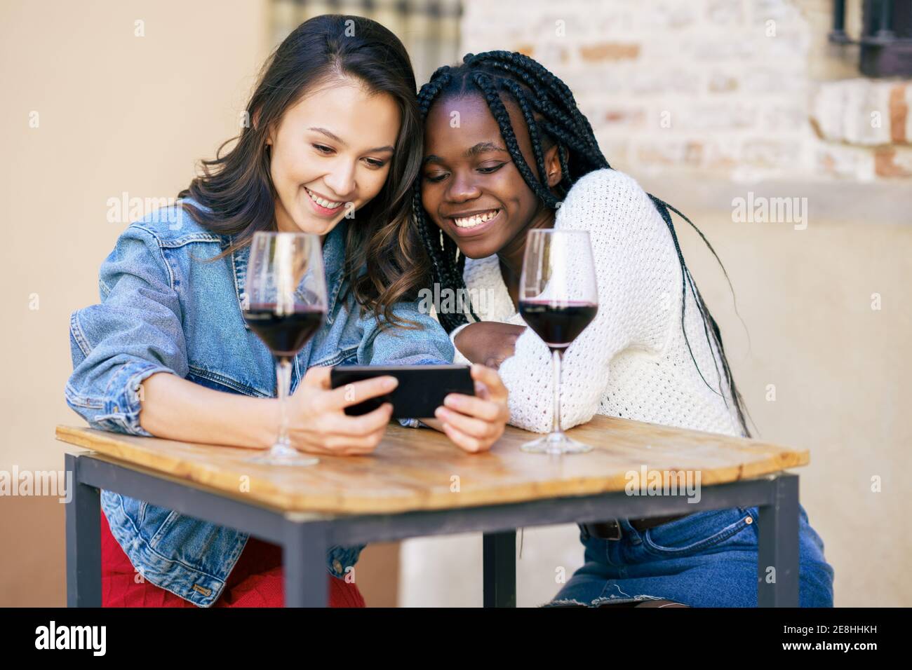 Deux femmes regardant leur smartphone ensemble tout en ayant un verre de vin. Banque D'Images