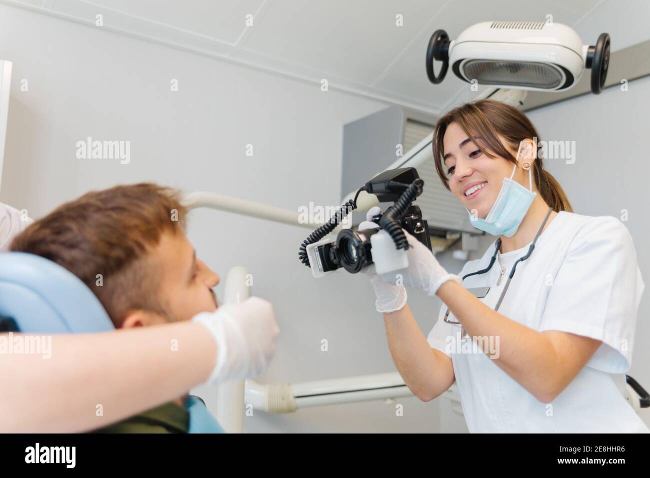Souriant dentiste femme compétent prenant des photos des dents de patient mâle tout en travaillant dans une clinique dentaire moderne équipée Banque D'Images