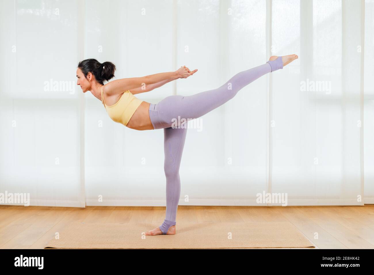 Vue latérale du corps entier de la femme qui s'étire les jambes pendant la flexion vers l'avant et en levant la jambe pendant les cours de yoga mixte Banque D'Images