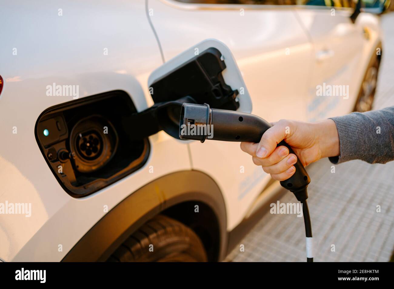 Vue latérale d'un homme court non reconnaissable tenant le câble à la fiche et rechargez la voiture électrique moderne dans la station-service en journée Banque D'Images