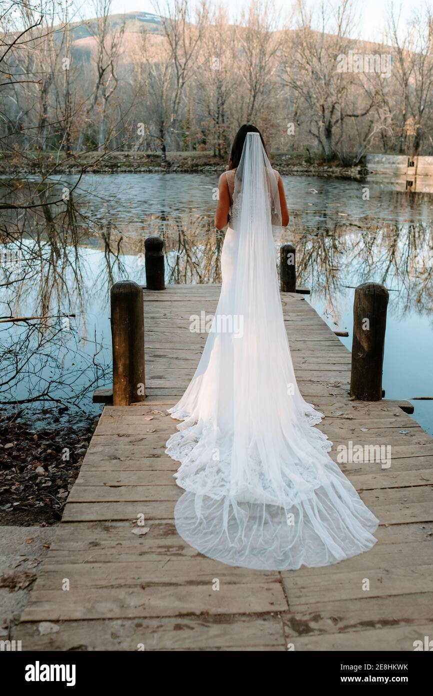 Vue arrière d'une jeune mariée élégante et blanche robe de mariage avec  voile long debout sur la jetée en bois près lac en forêt d'automne Photo  Stock - Alamy