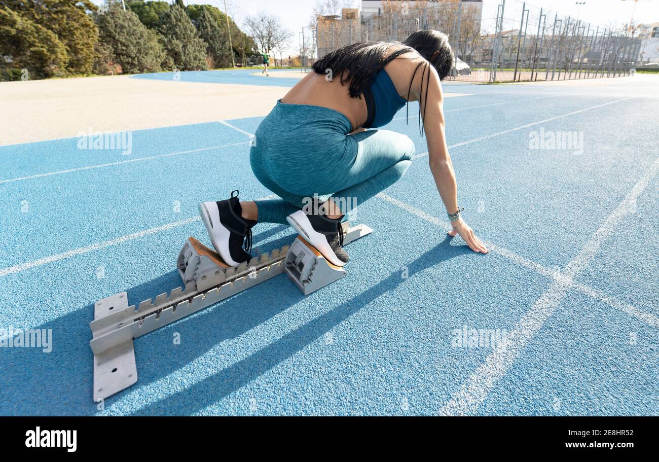 Vue latérale du Sportswoman assis dans des blocs de départ à crouch position de départ pendant l'entraînement au stade en été Banque D'Images