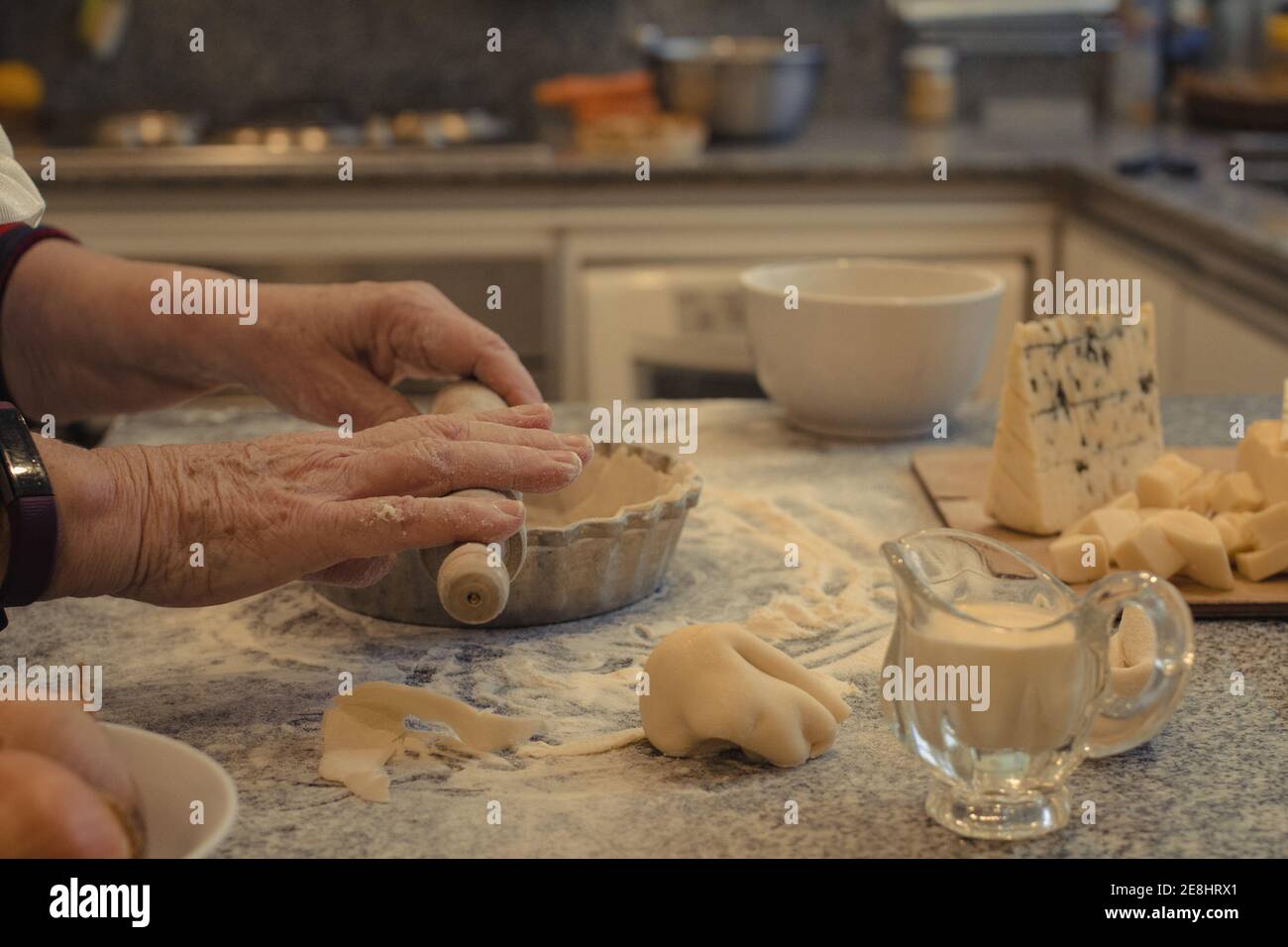 Crop anonyme chef avec pâte au-dessus de la table avec la cuisson plat et assortiment de fromages pendant la cuisson Banque D'Images