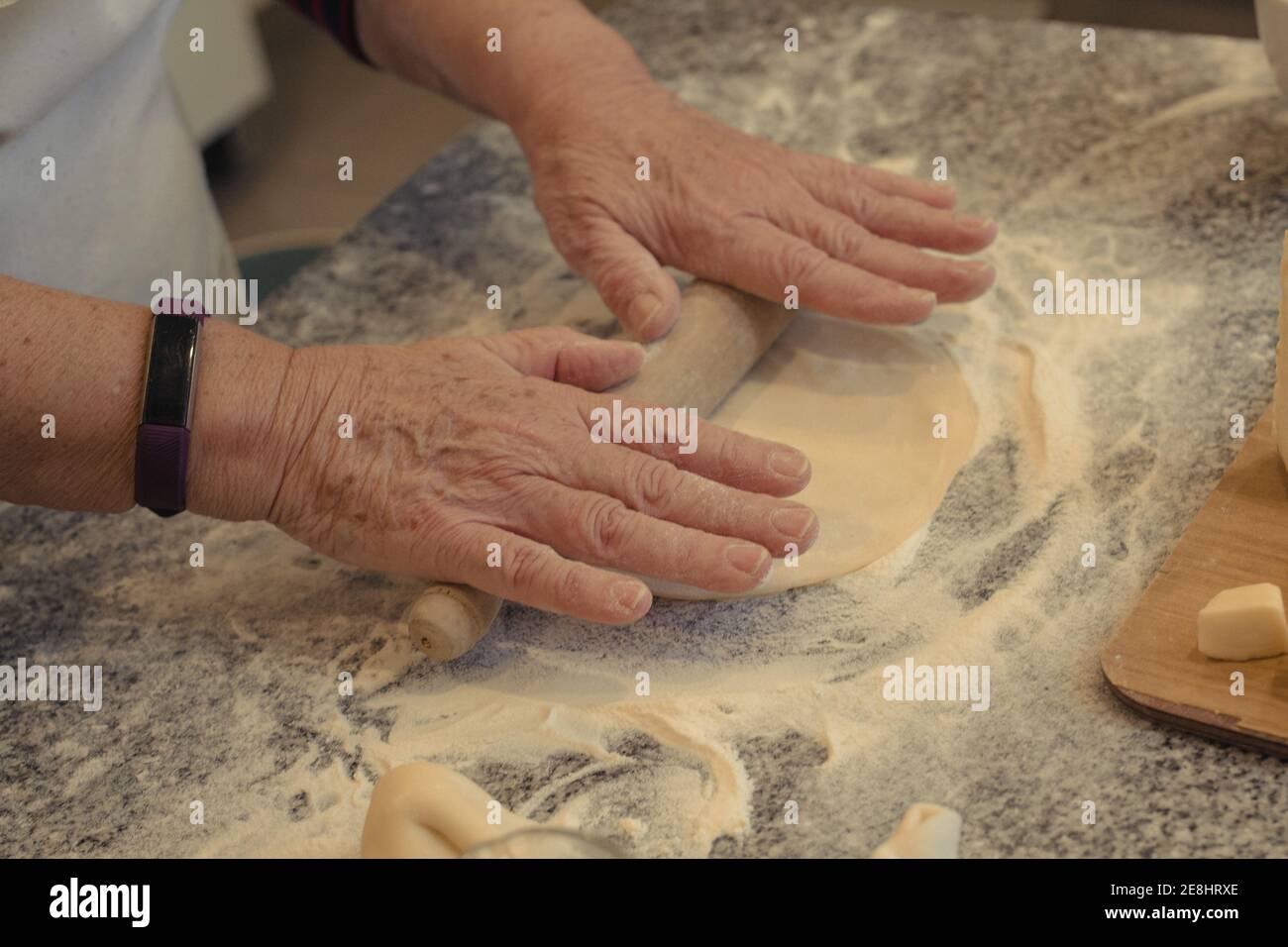 Du dessus de la récolte, les personnes âgées méconnaissables cuisent la croûte en roulant sur la table avec de la farine tout en cuisinant dans la cuisine à la maison Banque D'Images