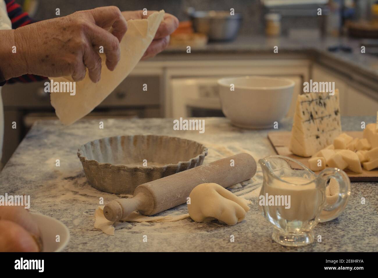 Crop anonyme chef avec pâte au-dessus de la table avec la cuisson plat et assortiment de fromages pendant la cuisson Banque D'Images