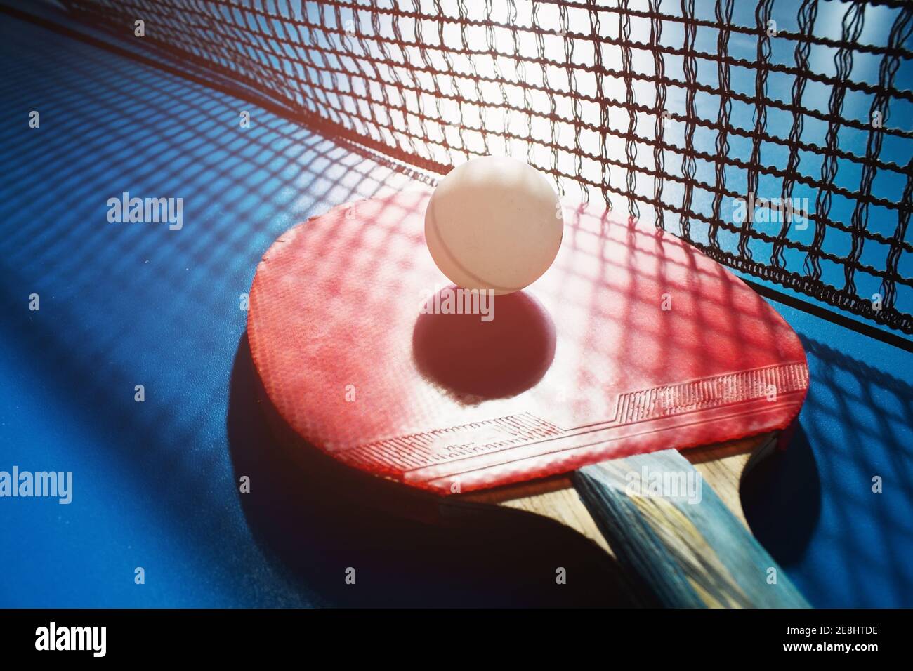 Une raquette de tennis de table rouge et une balle blanche reposent sur la surface de la table à côté du filet. Jeu de sport Banque D'Images