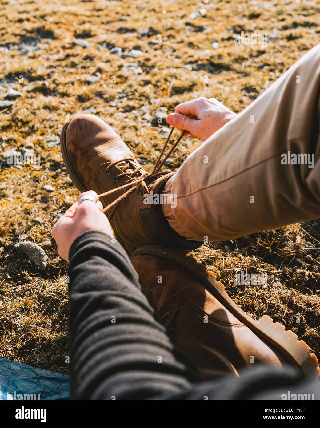 De dessus de crop anonyme homme randonneur dans une tenue élégante attacher les lacets des bottes en étant assis sur un sol herbeux jour ensoleillé Banque D'Images