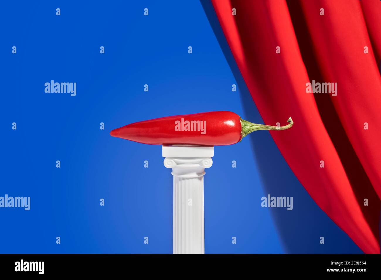 Le piment rouge est placé sur une colonne miniature sur fond bleu avec rideau en velours rouge Banque D'Images