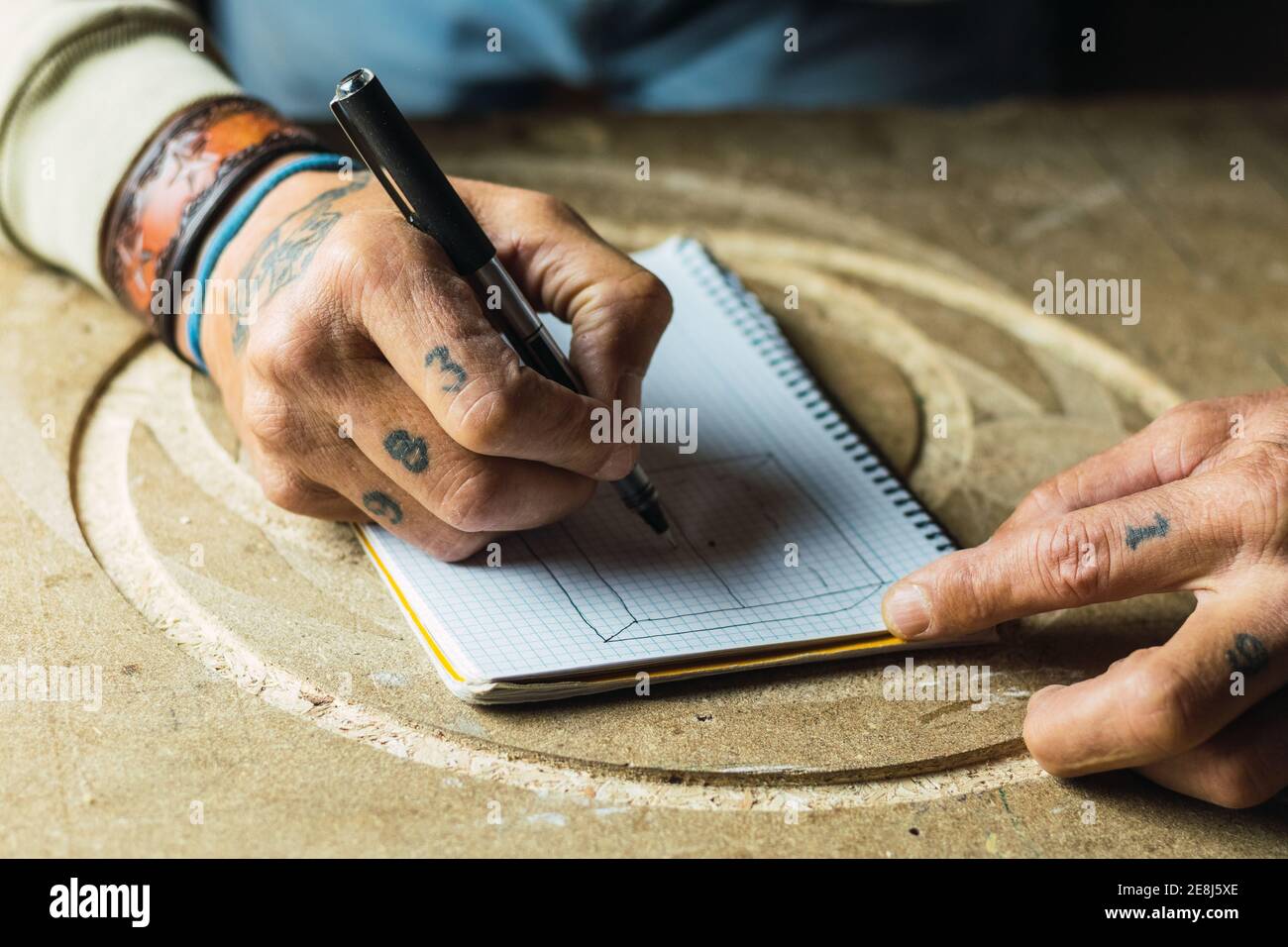 Grand angle de recadrage anonyme homme menuisier dessin esquisse dans bloc-notes assis à l'établi en menuiserie Banque D'Images